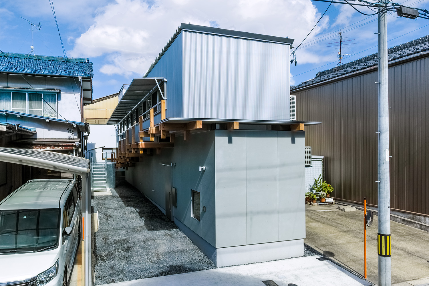 建物の東面と南面を同時に移した風景。２階部分には横へ一列に並ぶ窓。跳ね上げ式の雨戸が開けられている。