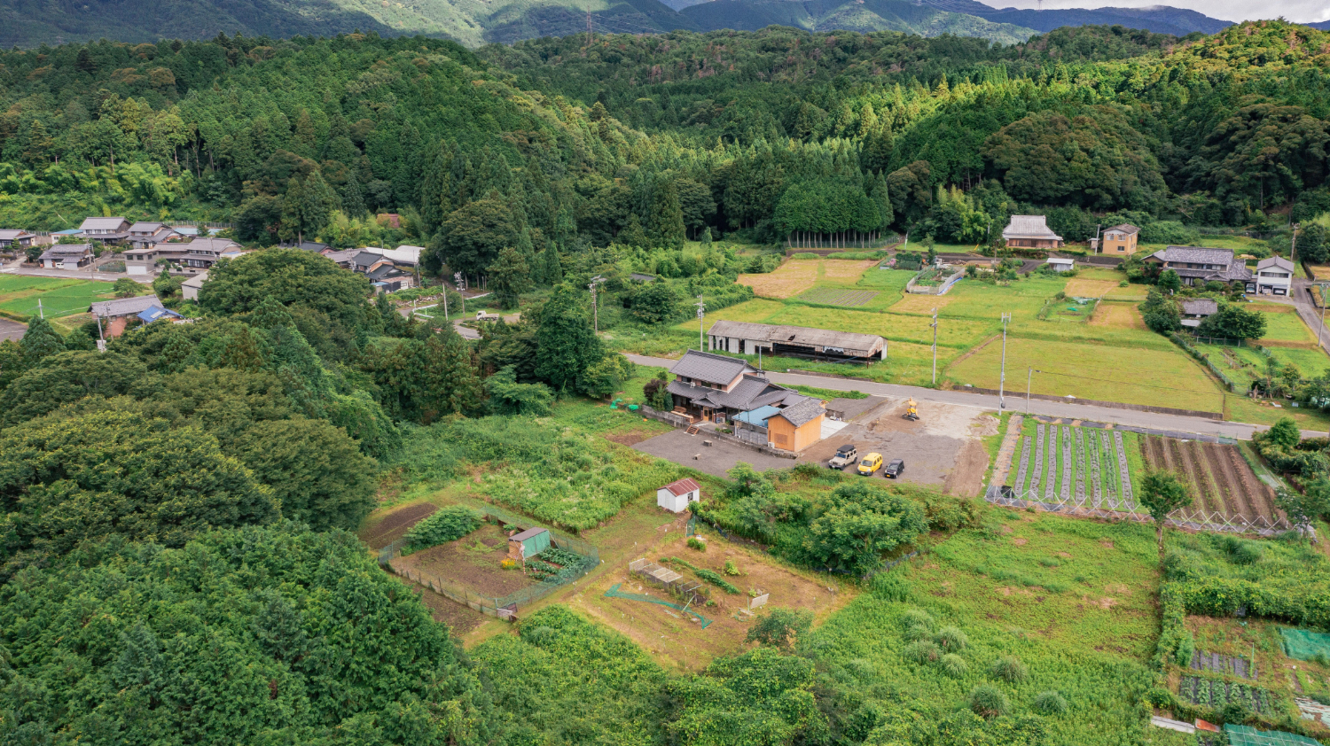 空撮風景。建設を中心に畑や山々が囲む。